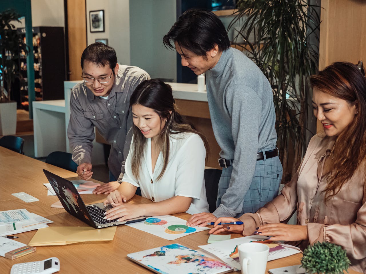 A group of colleagues engaged in a collaborative discussion around a laptop in a modern office.